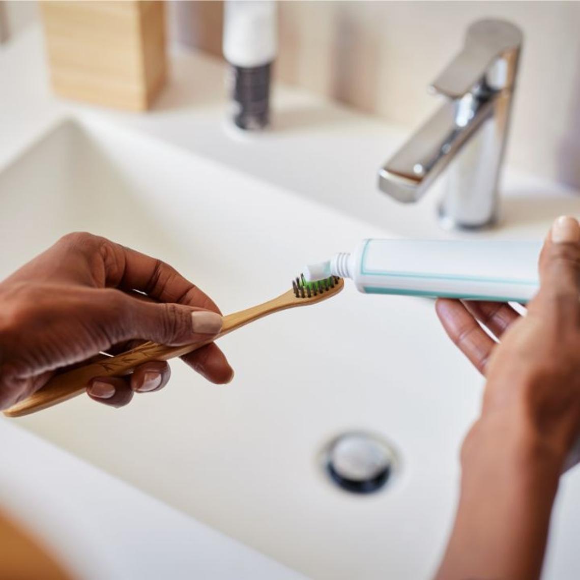 Toothpaste being put onto a toothbrush above a bathroom sink
