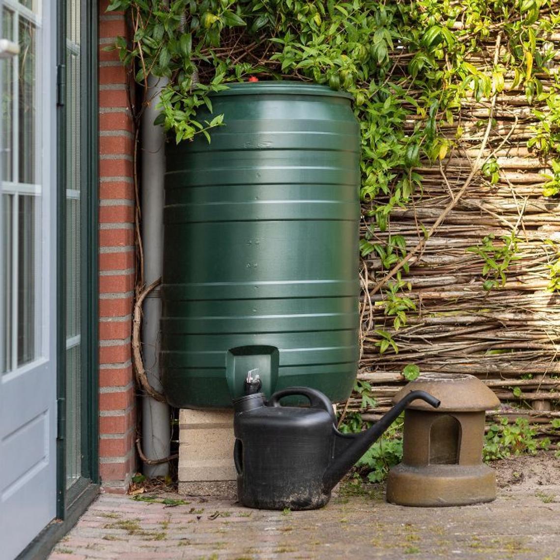 Green water butt next to a watering can on a garden patio