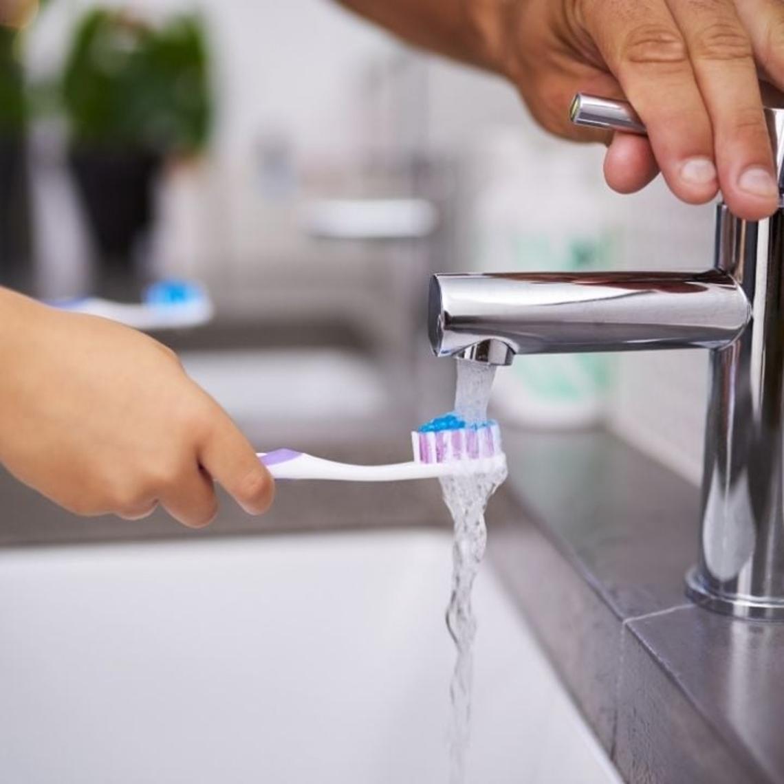 Parent switching on a bathroom tap with aerator for a child to wet their toothbrush