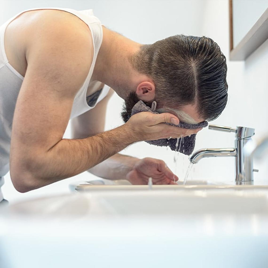 Man washing his face in the sink with a flannel
