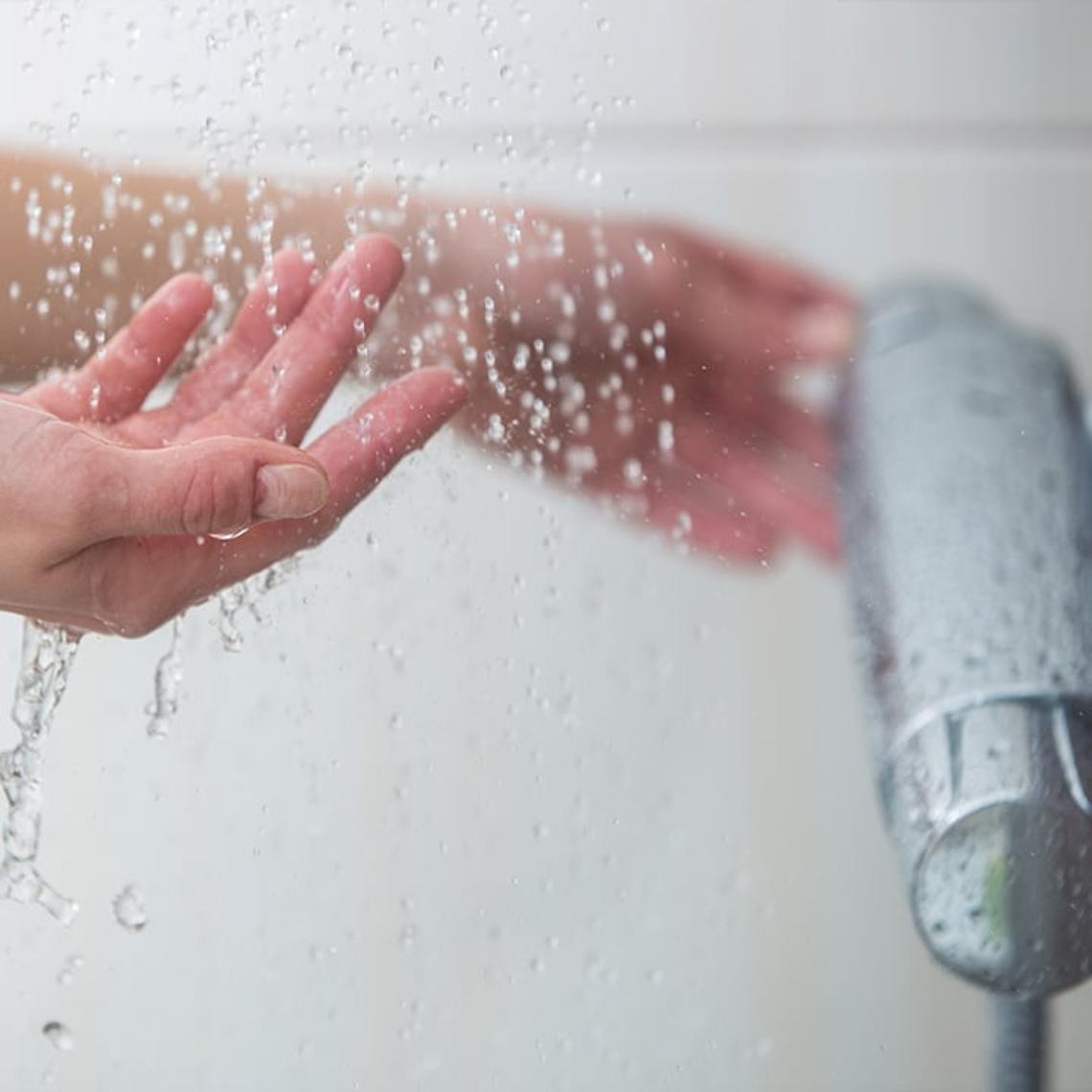 Photo of someone checking the water temperature in a shower