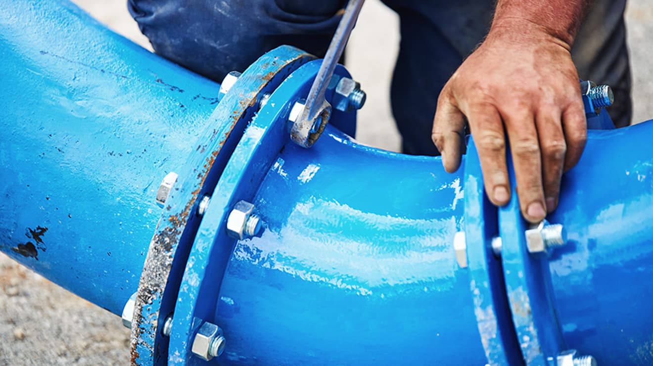 Man working on a large water pipe joint with a spanner