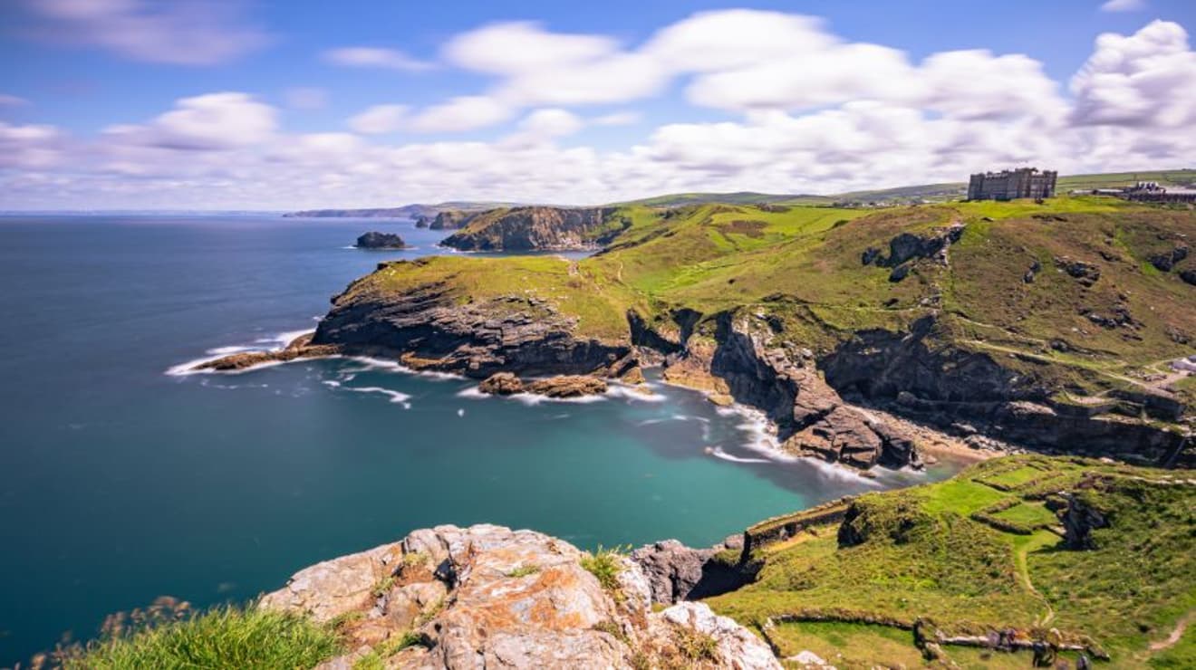 View of the red cliffs looking down to the sea with Tintagel castle in the background