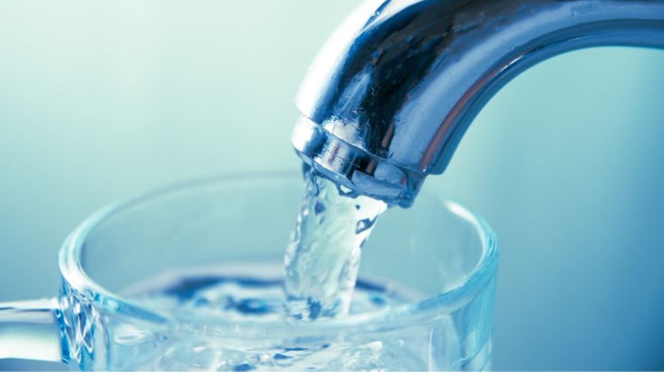Water pouring from a tap into a glass against a turquoise background