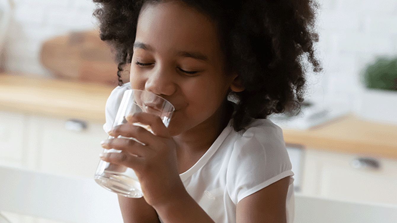 Little girl drinking water at the kitchen table
