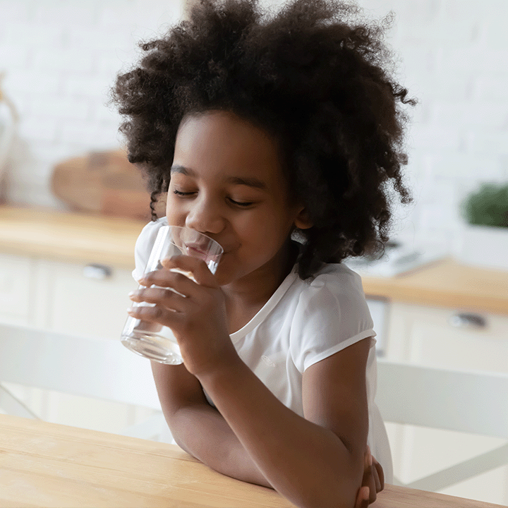 Little girl drinking water at the kitchen table