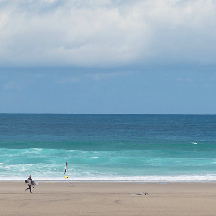 A surfer is running along a sandy beach towards the sea
