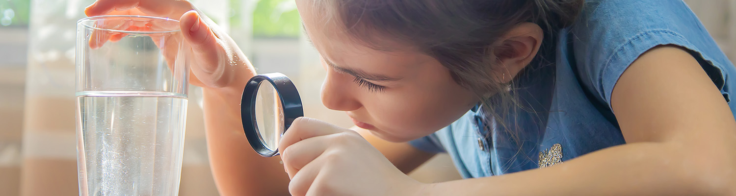 Young girl using a magnifying glass to look at a glass of water
